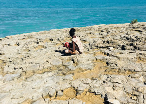 young male from youth justice program sitting on rocks at beach in broome