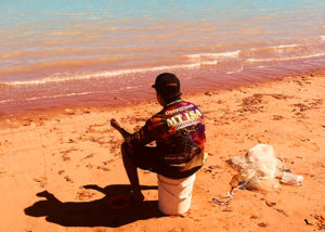 teenage male from youth justice program sits on the beach fishing in broome