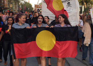 3 teenage girls marching with aboriginal flag
