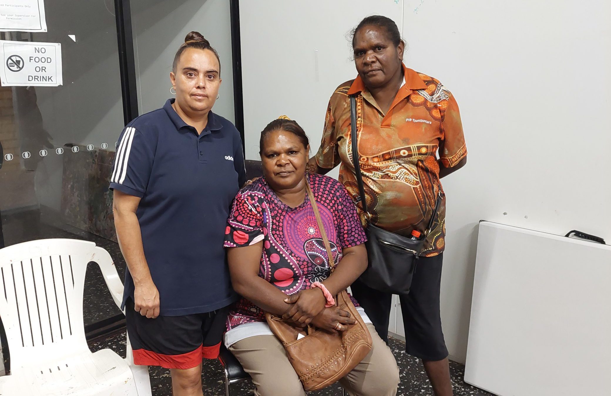 Three female participants of the Waalitj Foundation's Care Sector Traning. The one in the middle is seated; the two on either side of her are standing.